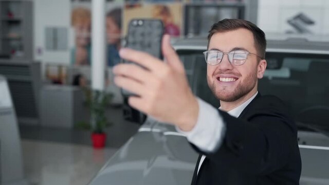 handsome man with glasses taking selfie with car on phone