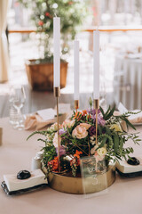 Wedding banquet. The festive table is decorated with compositions of flowers and greenery. On the table are glasses, talers with napkins, cutlery and name cards and menu cards.