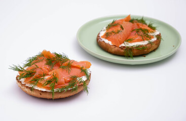 one half of a bun with smoked trout on a plate and the other on the table, decorated with fresh dill