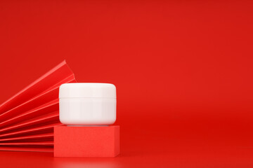 White cream tube on red podium against red background with copy space decorated with red waver. Concept of luxury or anti aging skin care products 