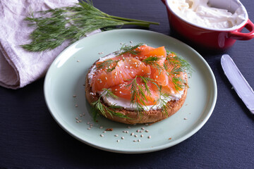 half bun greased with fresh cream, smoked fish and fresh dill on a plate and server board