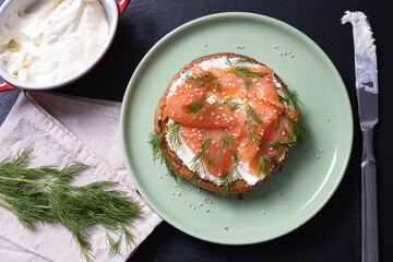 half a bun, oiled with fresh cream, garnished with smoked fish and sprinkled with fresh dill and sesame seeds, black background