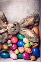Rustic,vintage wooden box with many colorful,painted easter eggs and wooden eggs with cute toy easter bunny in brown.