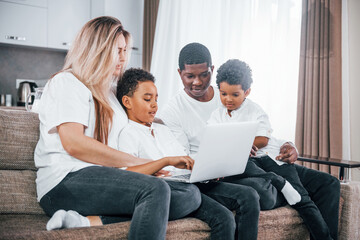 Fototapeta premium Multiracial family is together at home at daytime watching movie on laptop