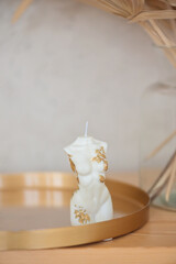 A trendy soy candle female body with a golden leaf on a dresser