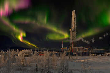 Winter landscape at polar night with a drilling rig. Northern oil and gas field. In the background there is a beautiful sky with northern lights