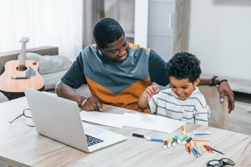 African american father with his son is indoors at home helping doing homework