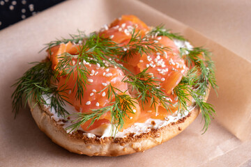 bun topped with fresh cream, garnished with smoked fish trout and sprinkled with fresh dill and sesame seeds on baking paper