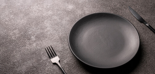 empty black plate, fork and knife on a dark background, horizontal photo, copy space