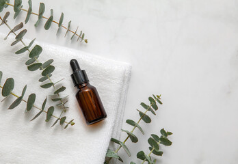 Amber glass cosmetic bottle with fresh eucalyptus leaves on marble background. Blank label for branding mock-up. Natural beauty product concept.	