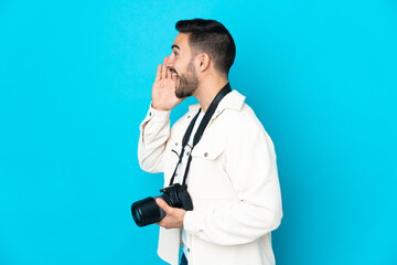 Young photographer man isolated on blue background shouting with mouth wide open to the side