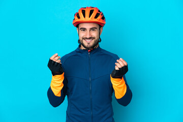 Young cyclist man isolated on blue background making money gesture - obrazy, fototapety, plakaty