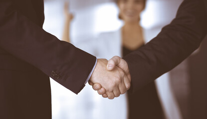 Unknown businesspeople are shaking their hands after signing a contract, while standing together in a modern office, close-up. Business communication, handshake, and marketing concept