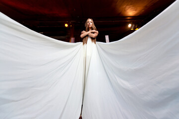 Young romantic elegant girl in long white flying dress posing on the stairs indoor
