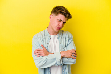 Young caucasian man isolated on yellow background frowning face in displeasure, keeps arms folded.