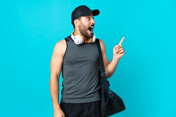 Young sport man with sport bag isolated on blue background intending to realizes the solution while lifting a finger up