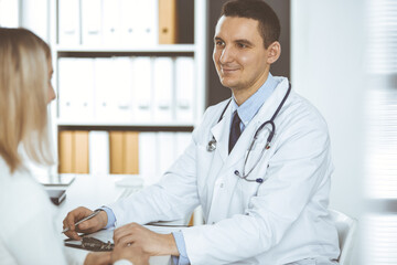 Friendly male doctor and patient woman discussing current health examination while sitting in clinic. Perfect medical service in hospital. Medicine and healthcare concept