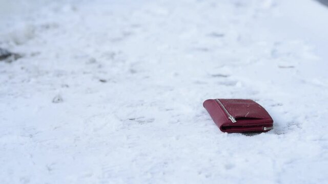 Close-up, wallet lies on ground in snow, find and a surprise, shoes snow on street in winter, loss loss of wallet, distraction not being attentive. Lose money wallet with credit cards documents.