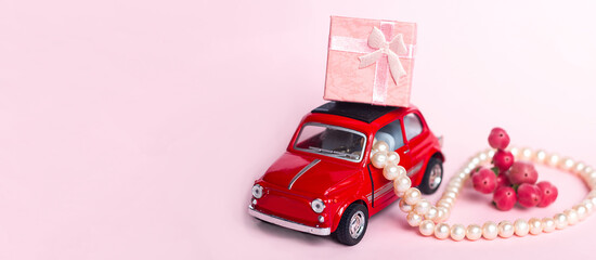 Red retro toy car delivers adefocused bouquet and a gift box on a blue background. Valentine's Day, February 14, greeting card. International Women's Day March 8, Mother's, copy space for text