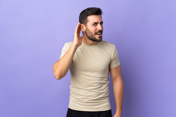 Young handsome man with beard over isolated background listening to something by putting hand on...