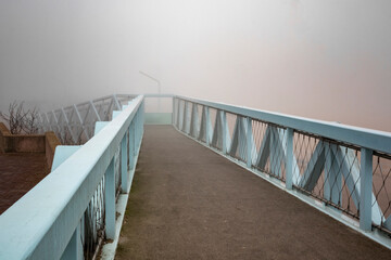 Peaceful empty road on a blue bridge into the fog