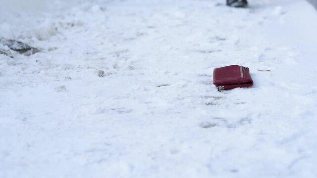 Close-up, wallet lies on ground in snow, find and a surprise, shoes snow on street in winter, loss loss of wallet, distraction not being attentive. Lose money wallet with credit cards documents.