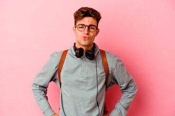 Young student man isolated on pink background blows cheeks, has tired expression. Facial expression concept.