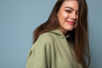 Obraz premium Young beautiful woman looking at camera. Trendy girl in casual hipster hoodie clothes. Positive female shows facial emotions. Funny model isolated on blue background with free space for text