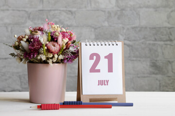 july 21. 21th day of the month, calendar date.A delicate bouquet of flowers in a pink vase, two pencils and a calendar with a date for the day on a wooden surface