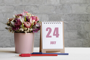 july 24. 24th day of the month, calendar date.A delicate bouquet of flowers in a pink vase, two pencils and a calendar with a date for the day on a wooden surface