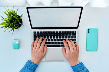 Person hands typing on keyboard at laptop with empty blank display during smart working online at minimalist desktop. Copy space, top view