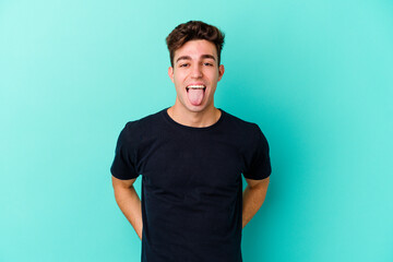 Fototapeta premium Young caucasian man isolated on blue background funny and friendly sticking out tongue.