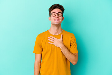 Young caucasian man isolated on blue background laughs out loudly keeping hand on chest.