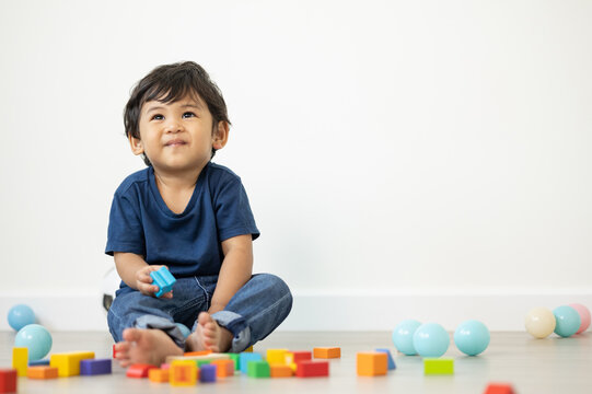 An Asian boy about 1 year old. Playing in the living room in the house He plays wooden toys in different colors. He is wearing a blue shirt.