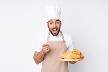 Male baker holding a table with several breads isolated on white background points finger at you