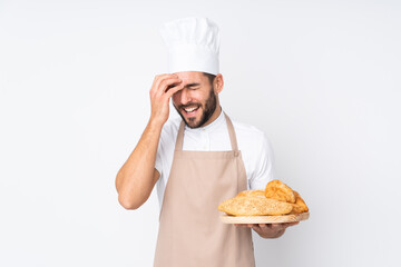 Male baker holding a table with several breads isolated on white background laughing