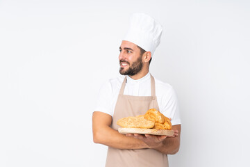 Male baker holding a table with several breads isolated on white background looking to the side