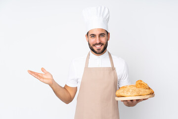 Male baker holding a table with several breads isolated on white background holding copyspace imaginary on the palm - obrazy, fototapety, plakaty