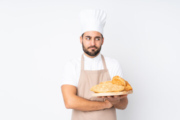 Male baker holding a table with several breads isolated on white background thinking an idea