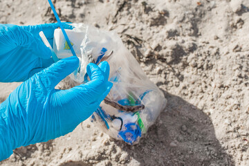Hands in protective rubber gloves lift and remove debris on the beach close up