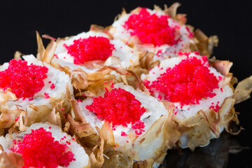 Sushi rolls with tuna or salmon shavings on a black background.