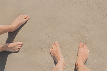 The legs of a guy and a girl stand on the wet beach sand by the sea, top view