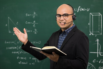 Young asian teacher man teaching video conference with student. Male Indian teacher training the mathematics in classroom from online course. He wearing small talk headset.