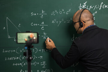 Indian young teacher man wearing headset teaching online video conference live stream by...