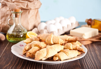 Freshly baked croissant on the plate with ingredients and kitchen utencil on the wooden table.