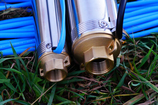Two borehole pumps with blue and black cables lie on the grass. Submersible well pumps close-up. Inlet thread of borehole pumps.