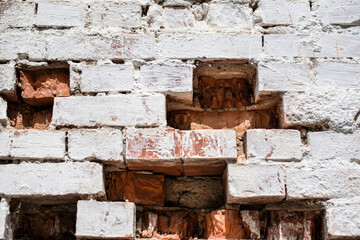 The old brick wall is painted white, a few bricks have already fallen out of the wall, a beautiful background of an old brick wall