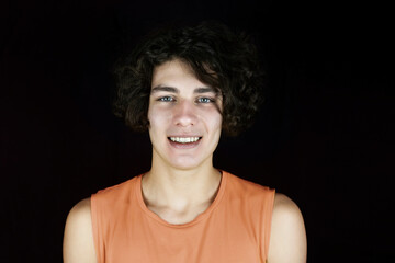 Portrait of a happy teenage boy who sincerely smiles, has dark curly hair and white healthy teeth....