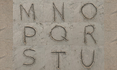character M N O P Q R S T U hand written on sand in evening
