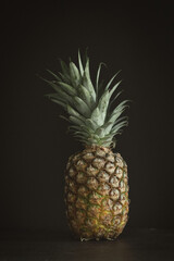 Vertical still life of a pineapple on a dark background. Dark moody food photography style. Studio shot with copy space.